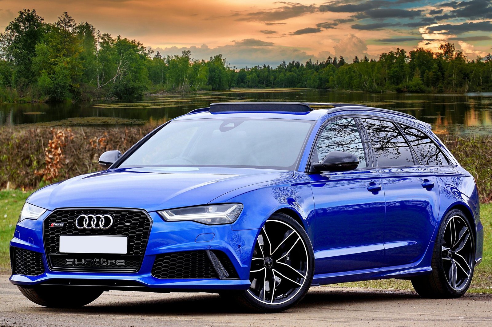 A modern blue Audi RS6 parked by a lake with scenic forest and sky backdrop.